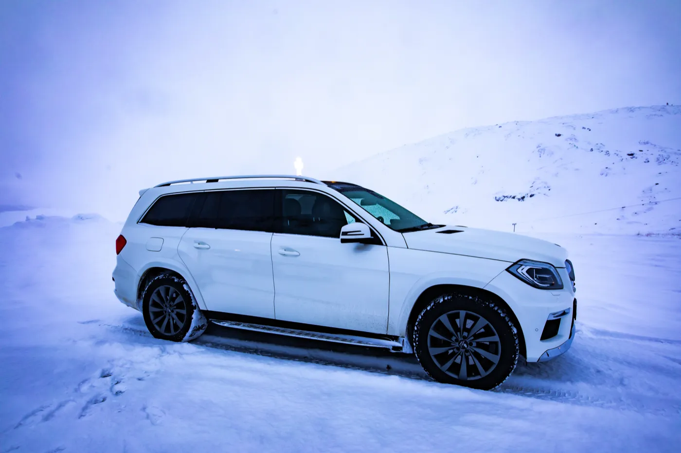 Hvit Mercedes-bårebil fra siden i vinterlys