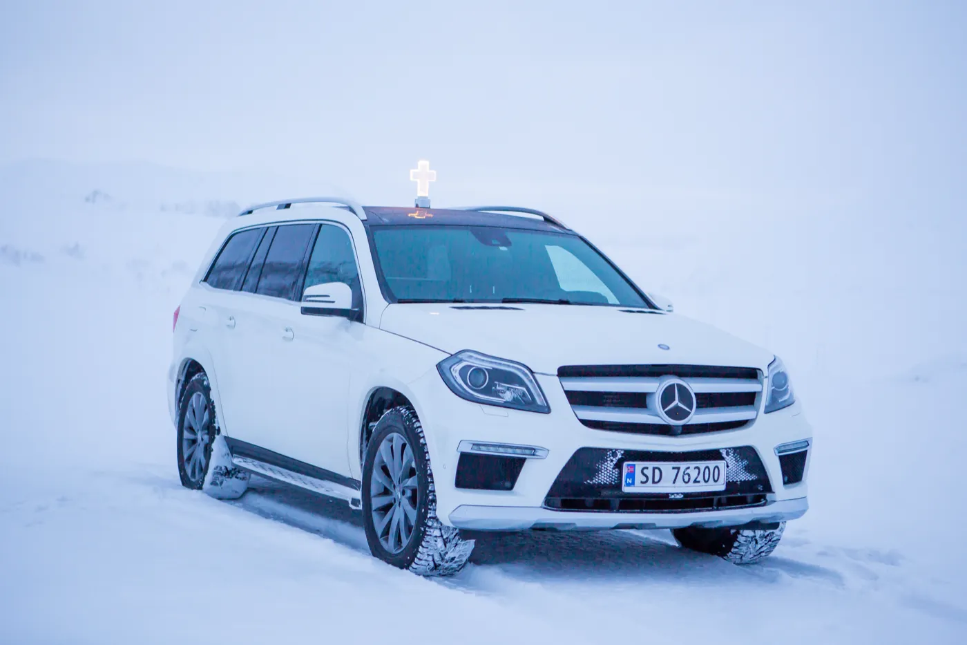 Hvit Mercedes-bårebil forfra i snø, med kors på taket
