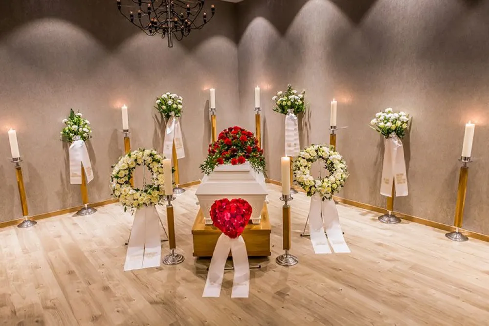 Blomsterkranser og tente lys rundt en kiste
