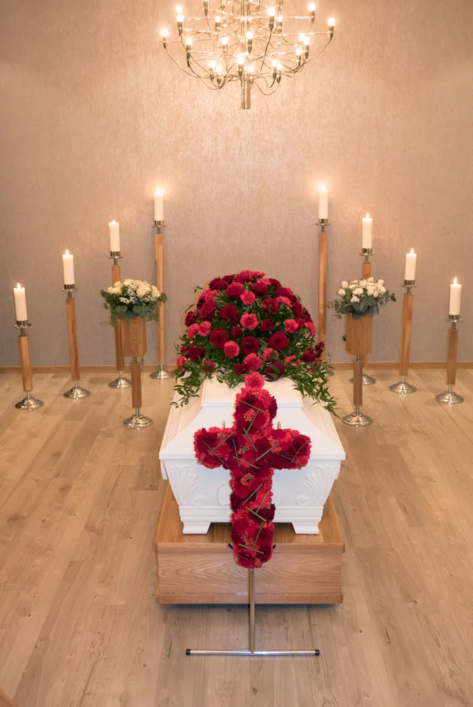 Hvit kiste med rødt blomsterkors, omgitt av tente lys i IMIs seremonirom