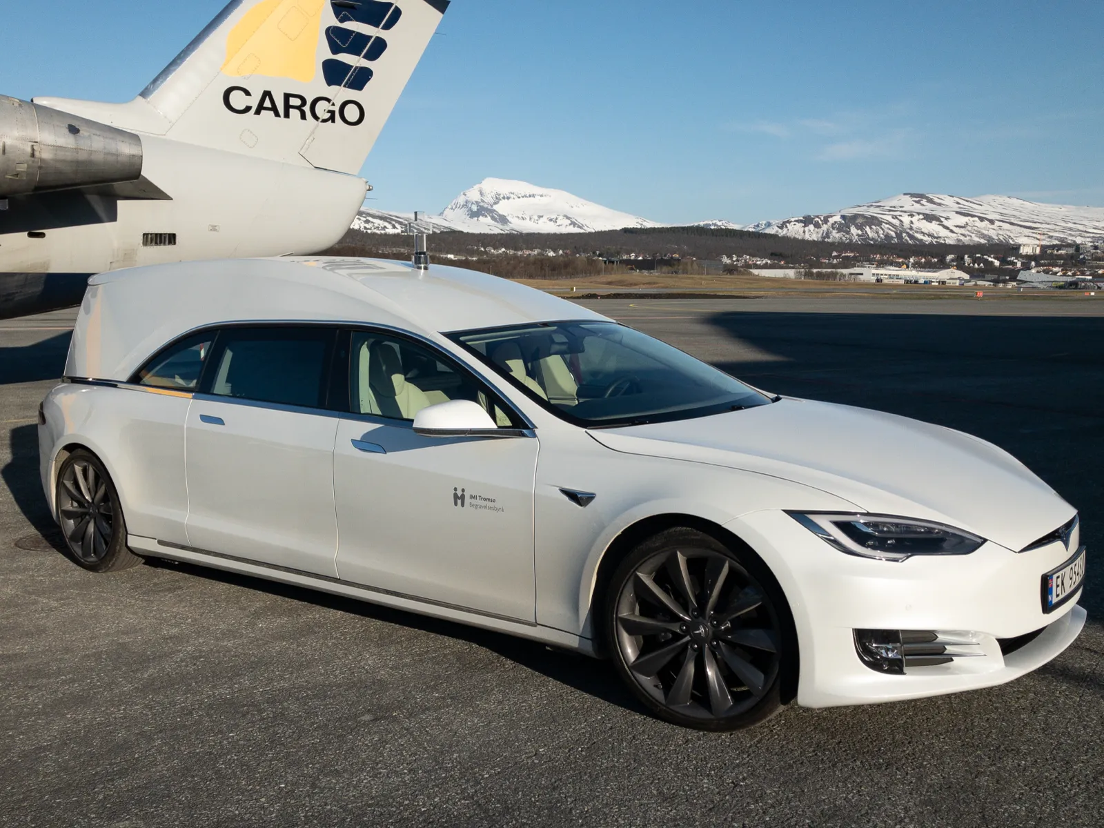Teslaen ved et fraktfly, med snødekte fjell i bakgrunnen
