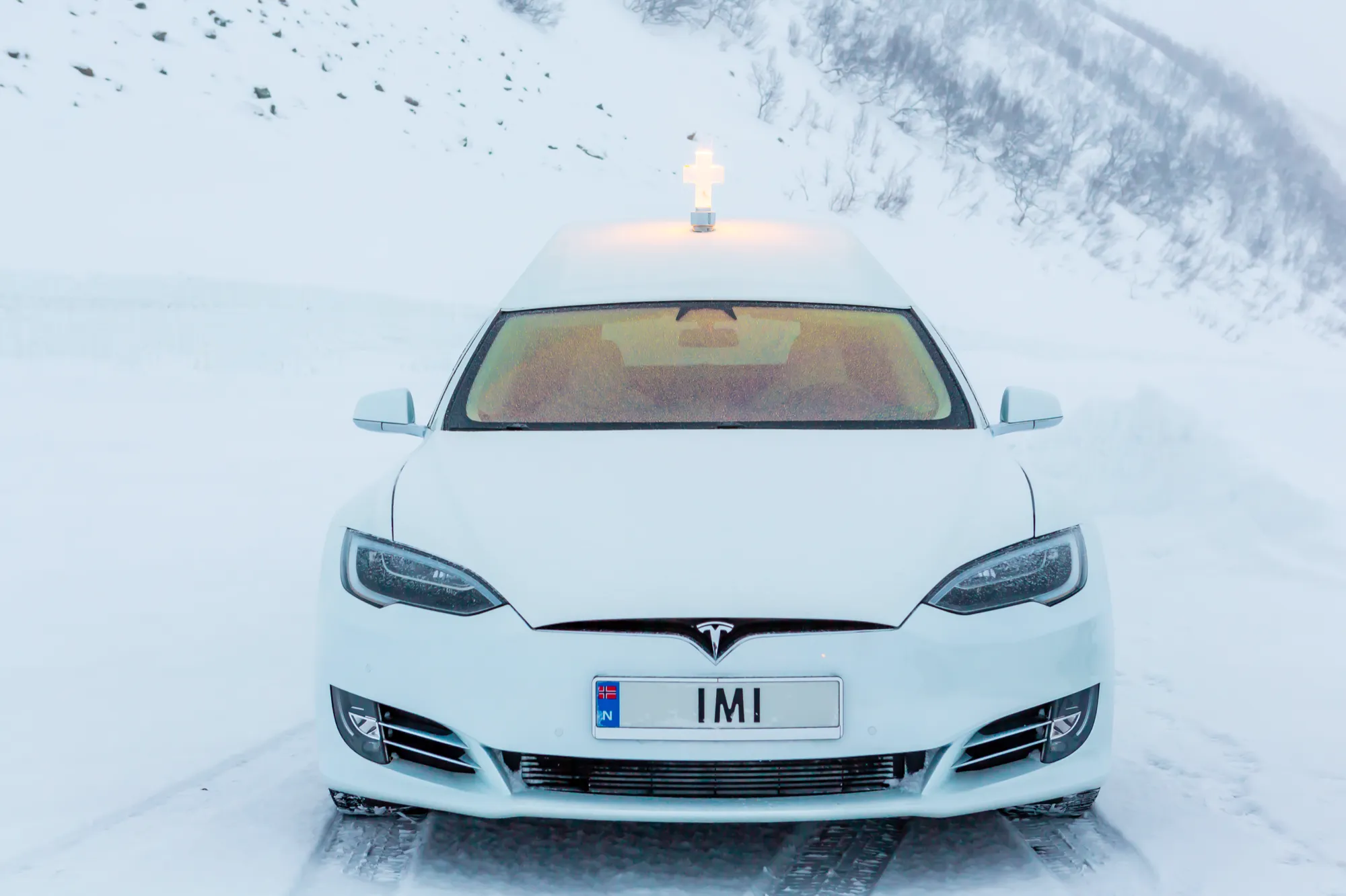 Teslaen forfra i snø, med IMI på skiltet