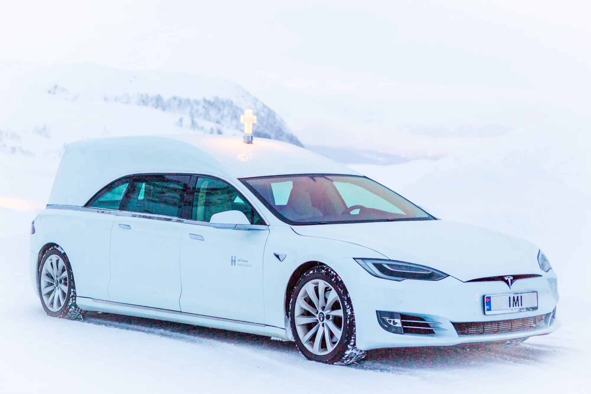 IMIs hvite Tesla-bårebil med kors på taket, parkert i snøen
